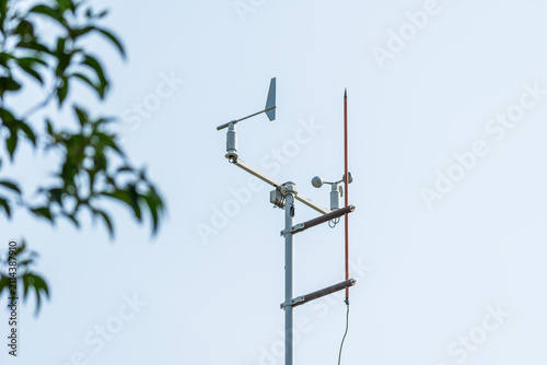 Quadro su tela Weather monitoring instruments including anemometer and wind vane mounted on a metal pole, with a tree branch in the background