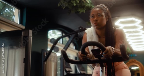 Focused Black woman rides a stationary bike during an indoor cardio workout in a modern gym.