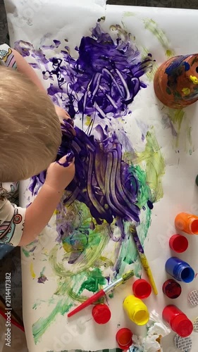 Young Child Making Messy Purple Finger Painting, Overhead View - Vertical overhead footage of a young child pouring and spreading thick purple paint across paper with paint-covered hands during a colo