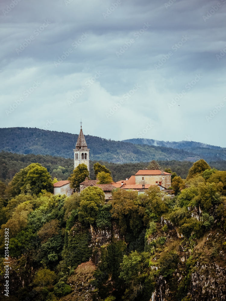 Fototapeta premium Hilltop Village Beneath Dramatic Storm Clouds in Slovenia
