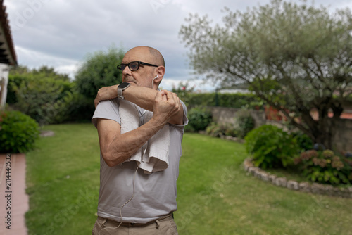 Senior Man Stretching in Garden With Headphones and Smartwatch Preparing for Outdoor Exercise