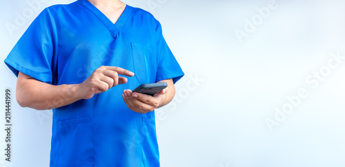 Fotografie Closeup of a medical professional wearing blue scrubs and using a smartphone wit