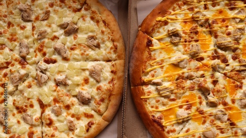 Two delicious round pizzas in boxes. On the left is a chicken fillet, juicy pineapple, and mozzarella. On the right is a chicken fillet with melted cheddar and zigzags of yellow sauce.