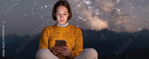 Young woman using smartphone outdoors at night under starry sky representing digital detox connection and modern lifestyle balance.