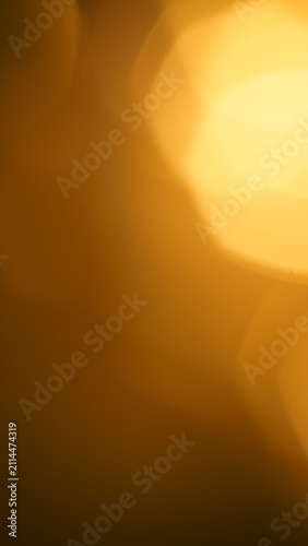 Close up of a large warm golden bokeh light orb diffusing across a dark vertical background.
