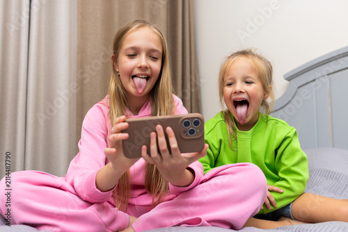 Quadro su tela Two young girls making funny faces while watching something on a smartphone at h