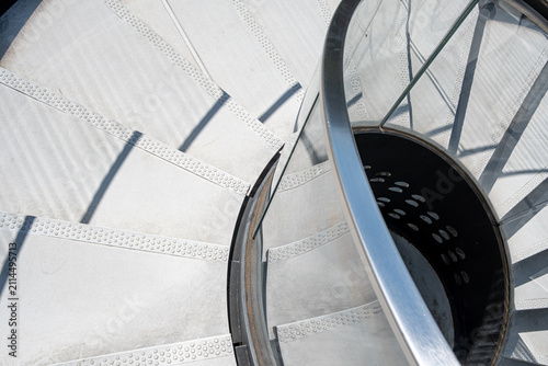 An overhead view follows a spiral staircase, where a railing circles the steps as layered shadows turn interior architecture into sweeping curves and geometry across the frame