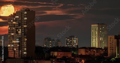 Massive orange full moon setting behind city skyscrapers and clouds time lapse