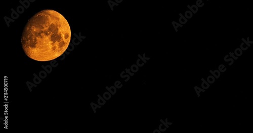 Massive orange moon setting behind tv tower silhouette at night time lapse