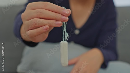 Woman's hand dangling clean white cotton tampon by its blue string