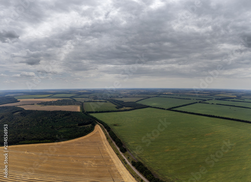 Aerial summer fields with dark dramatic sky. Landscape with agriculture patterns from drone