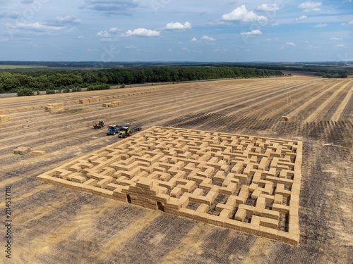 Summer fair maze from hay bales on harvested wheat field with tractors work in rural scenery
