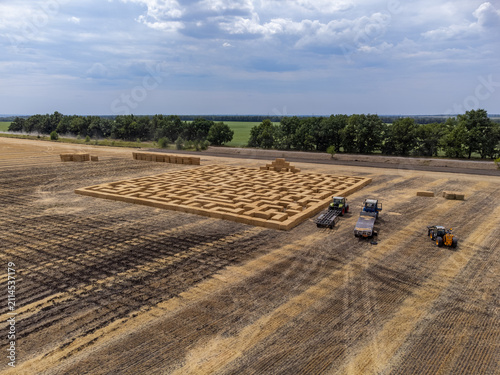 Wheat bales maze with tractors on harvested wheat field. Agricultural summer fair in rural landscape
