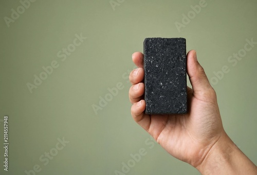 A hand holding a black textured bar of charcoal soap