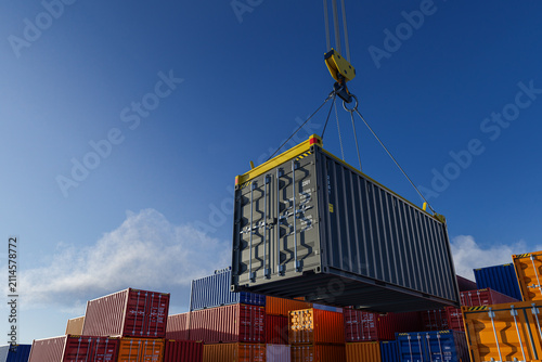 Industrial crane lifting cargo container high in blue sky at port