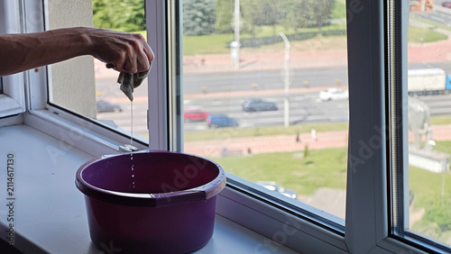 Fotografie Hand wringing out a damp cloth into a purple basin, cleaning apartment window ov