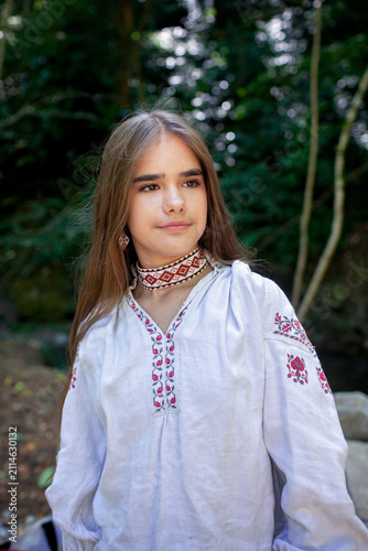 Young Ukrainian woman in embroidered clothing showing her long natural hair in a sunlit forest, combining feminine beauty, cultural tradition and nature.