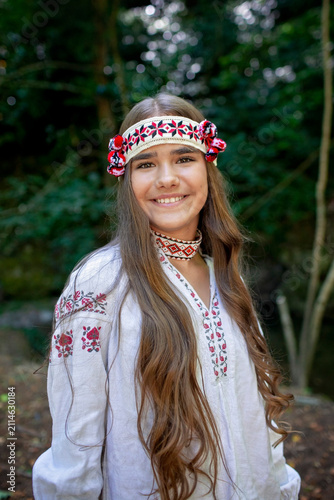 Young Ukrainian woman in embroidered clothing showing her long natural hair in a sunlit forest, combining feminine beauty, cultural tradition and nature.
