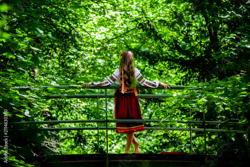 Young Ukrainian woman in traditional embroidered clothing crossing a forest bridge, symbolizing cultural roots, personal journey, continuity and transition.