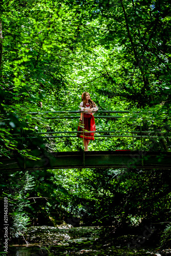 Young Ukrainian woman in traditional embroidered clothing crossing a forest bridge, symbolizing cultural roots, personal journey, continuity and transition.