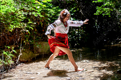 Young Ukrainian woman in embroidered traditional clothing sitting beside a clear forest stream, expressing serenity, cultural identity and connection with nature.