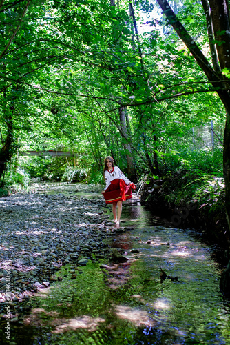 Young Ukrainian woman in embroidered traditional clothing sitting beside a clear forest stream, expressing serenity, cultural identity and connection with nature.
