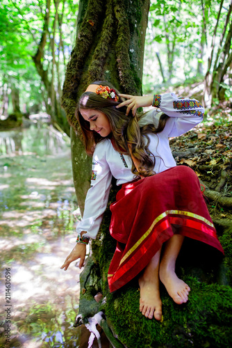 Young Ukrainian woman in embroidered traditional clothing sitting beside a clear forest stream, expressing serenity, cultural identity and connection with nature.