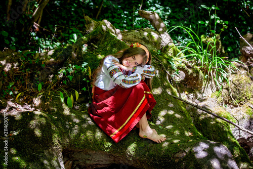 Young Ukrainian woman in a traditional embroidered costume standing in a green forest, combining cultural heritage, femininity and a close connection with nature.