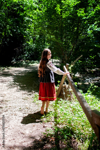 Young Ukrainian woman in a traditional embroidered costume standing in a green forest, combining cultural heritage, femininity and a close connection with nature.