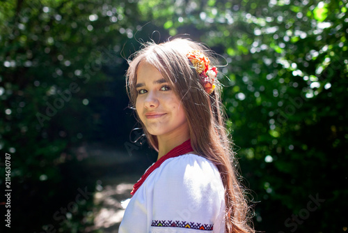 Young Ukrainian woman in a traditional embroidered costume standing in a green forest, combining cultural heritage, femininity and a close connection with nature.