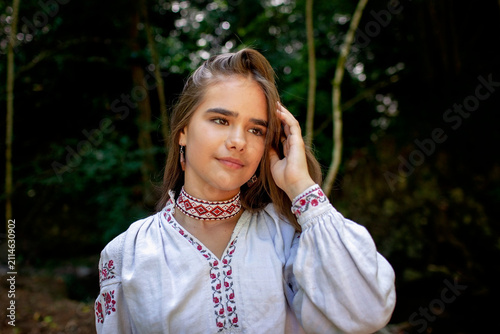 Portrait of a young Ukrainian woman in traditional embroidered clothing and folk accessories in a green forest, representing culture, heritage and national identity.