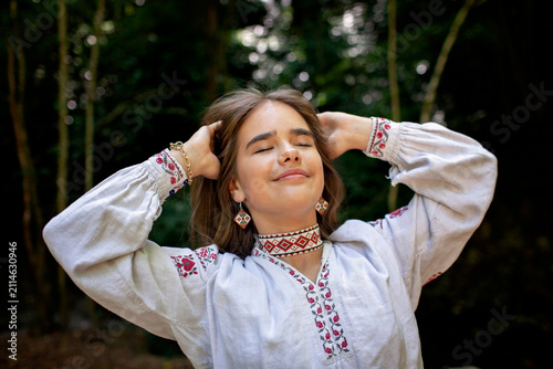 Portrait of a young Ukrainian woman in traditional embroidered clothing and folk accessories in a green forest, representing culture, heritage and national identity.