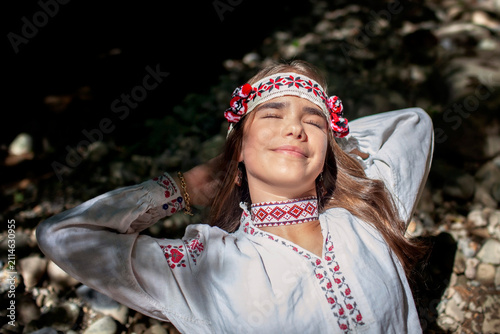 Portrait of a young Ukrainian woman in traditional embroidered clothing and folk accessories in a green forest, representing culture, heritage and national identity.