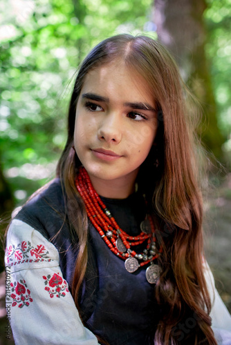 Portrait of a young Ukrainian woman in traditional embroidered clothing and folk accessories in a green forest, representing culture, heritage and national identity.