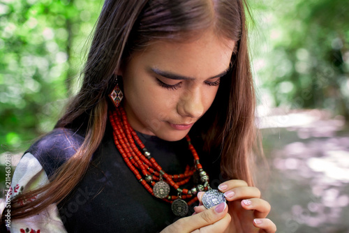 Portrait of a young Ukrainian woman in traditional embroidered clothing and folk accessories in a green forest, representing culture, heritage and national identity.