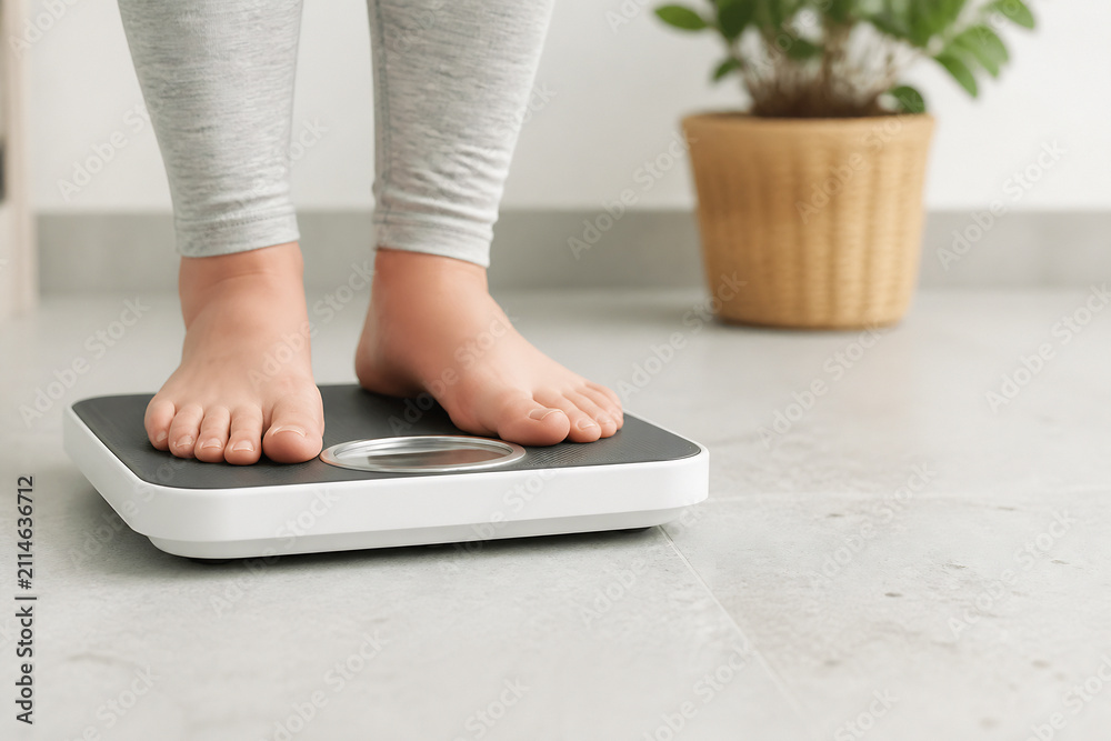 Fototapeta premium A person's bare feet are standing on a digital bathroom scale in a bright, indoor setting.
