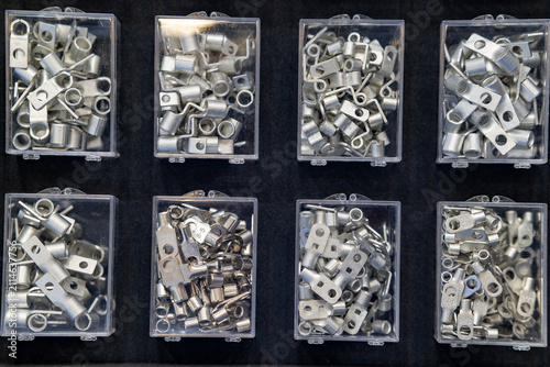Metal cable lugs organized in transparent plastic boxes.