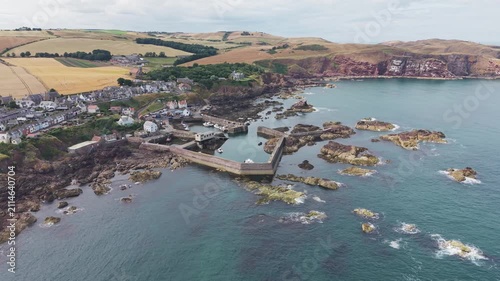 Scenic semi-circular pan left to right over St Abbs fishing harbour and coastal village, showcasing the dramatic rocky shore and North Sea coastline in Berwickshire, Scotland