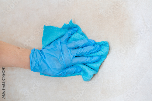 Close-up of a hand in a blue rubber protective glove wiping and cleaning ceramic wall tiles with a microfiber cloth