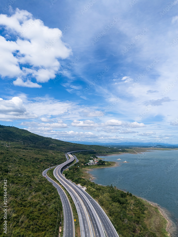 Obraz premium Drone aerial view of a highway running beside a reservoir with lush green mountains, Transportation infrastructure and renewable energy concept