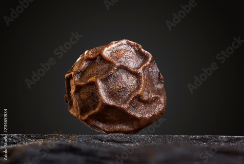 Single Black Peppercorn Standing on Dark Background
