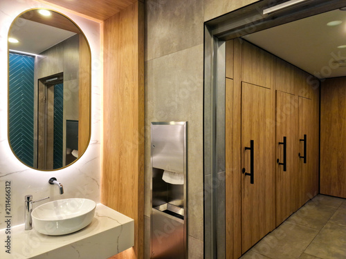 Luxury public restroom interior with backlit oval mirror and wooden cubicles