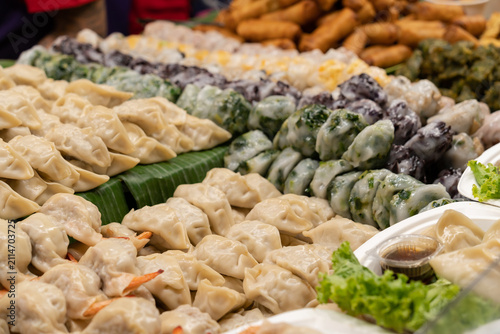 A close-up view of assorted handmade dumplings, spring rolls, and traditional Asian snacks neatly displayed on banana leaves at a local food market.