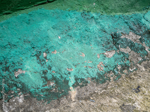 Close-up of a weathered concrete wall with peeling turquoise paint, revealing rough grey plaster texture, cracks, and natural grunge details.