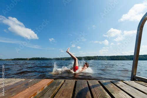 Obraz na plátně Man falls off a wooden dock into a lake splashing water on a summer day