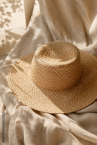 Elegant woven straw sun hat on soft linen fabric with warm natural light and minimalist summer aesthetic