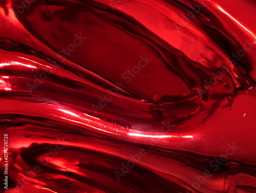 Close-up of a glossy, reflective red metallic surface with smooth fluid waves, bright highlights, and deep shadows creating an abstract, dynamic texture.