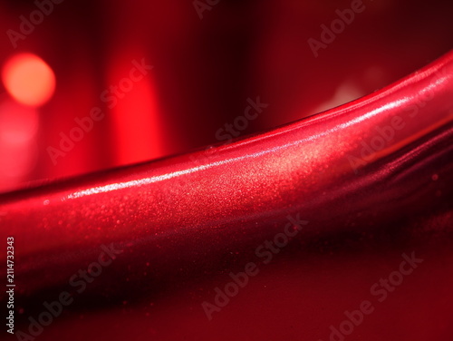 Close-up of a smooth, glossy metallic red surface with a sharp bright highlight line and a soft bokeh background creating an abstract, modern aesthetic.