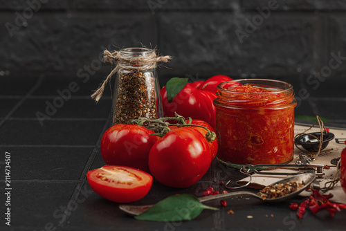 Homemade tomato sauces, ketchup and adjika in glass jars with heirloom tomatoes on dark background