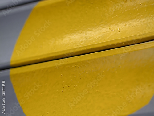 Close-up of a textured yellow painted metal surface with small surface bubbles and a distinct panel gap against a grey background.